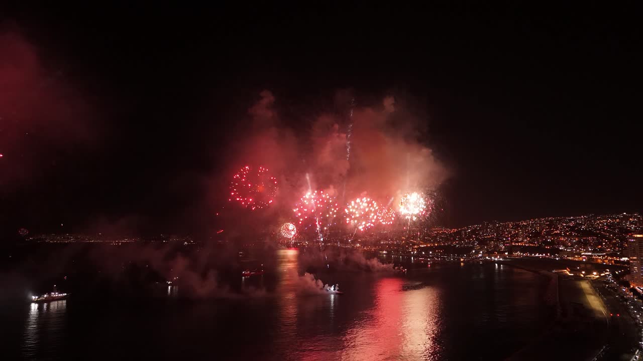 Dolly out flyover of the city of Valparaiso Chile at night with ships on the coast - fireworks at the New Year's Eve show