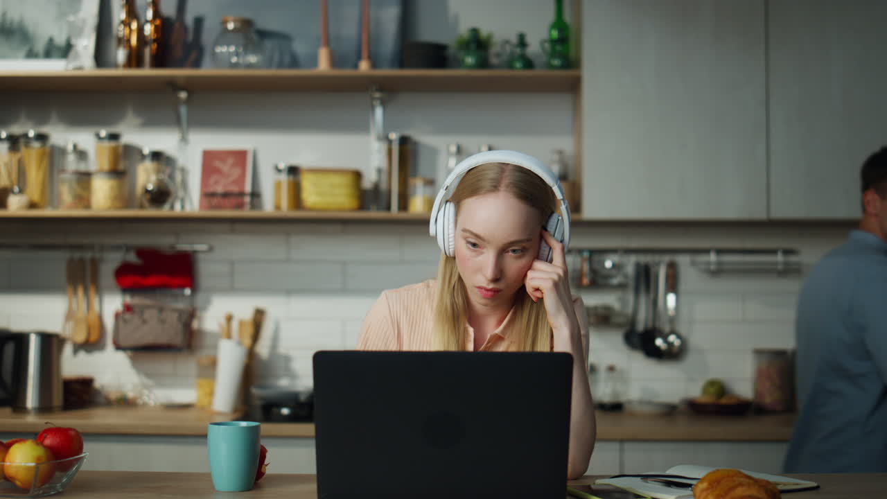 Woman accountant working remotely sitting at kitchen with headphones close up.