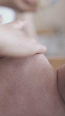 little boy with short fair hair in white diaper lies on side and skilled nurse performs arm massage close view