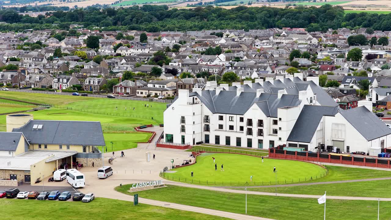 Drone hovers over golf clubhouse, putting green, and town buildings on a bright summer day