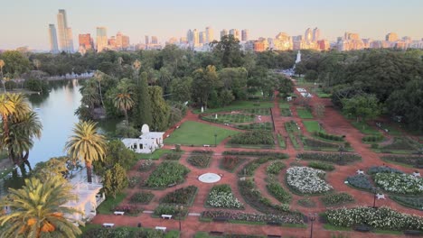 aerial jib up over rosedal gardens near pond in palermo neighborhood, skyline in background at sunset, buenos aires