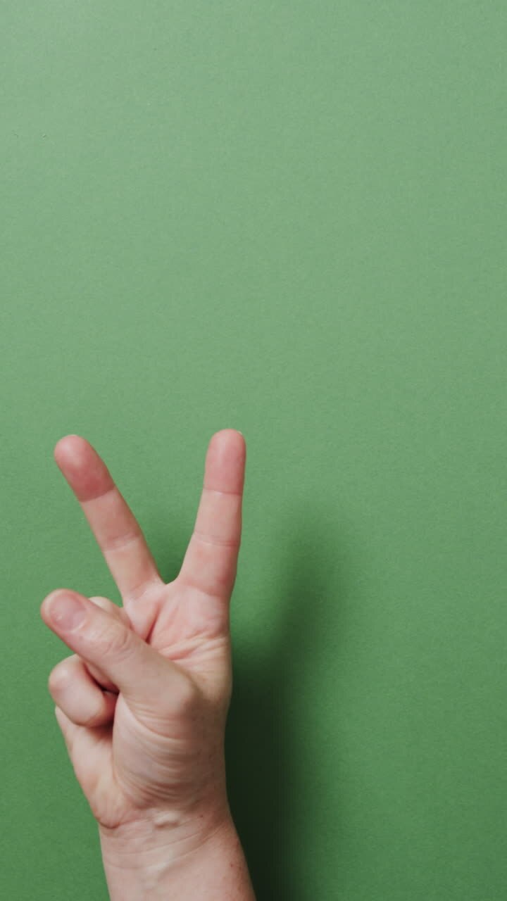 Video verticale della mano di un uomo caucasico che mostra il segno della pace con spazio per il testo su sfondo verde