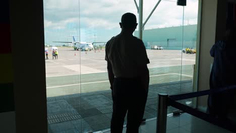 Un-Piloto-De-Silueta-Mirando-Un-Avión-Desde-Dentro-Del-Aeropuerto-4k