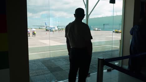 a silhouette pilot looking at an aircraft from inside the airport 4k