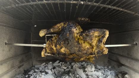 rotisserie chicken rotating in a wood and charcoal fire brick bbq grilling in slomo