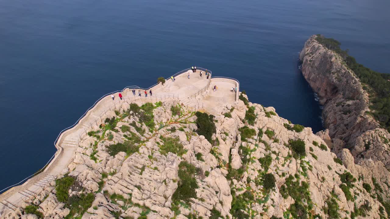 A cliff with a path leading to a viewpoint. Tourists enjoy the view at Cap de Formentor