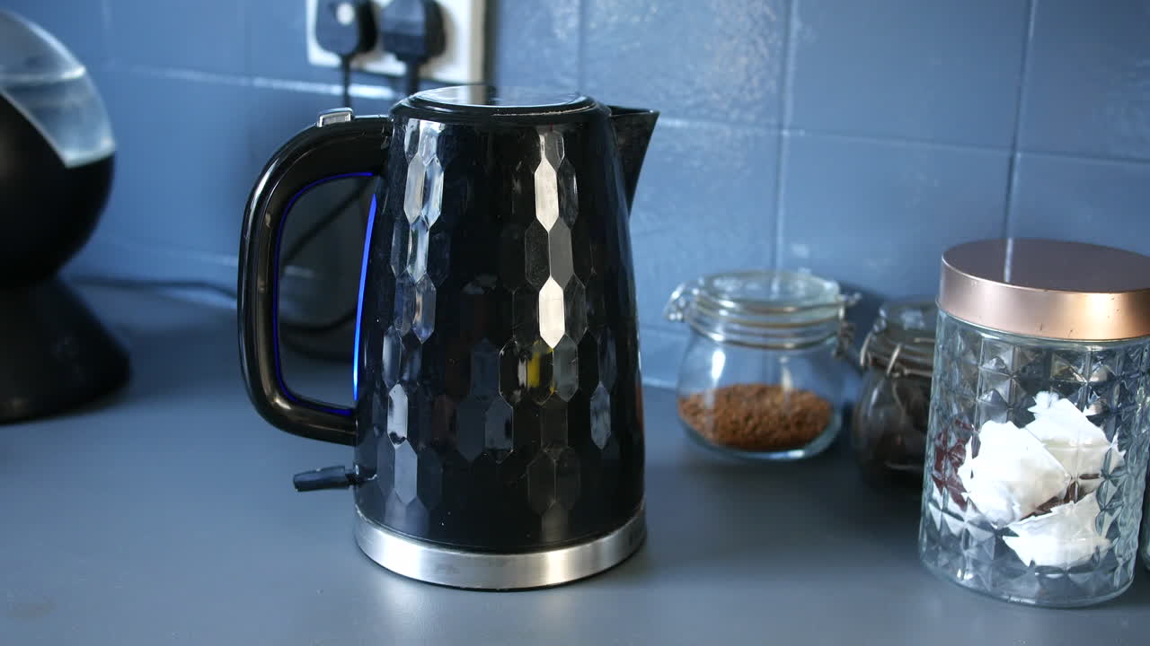 A man switching on an electric kettle in a kitchen at home