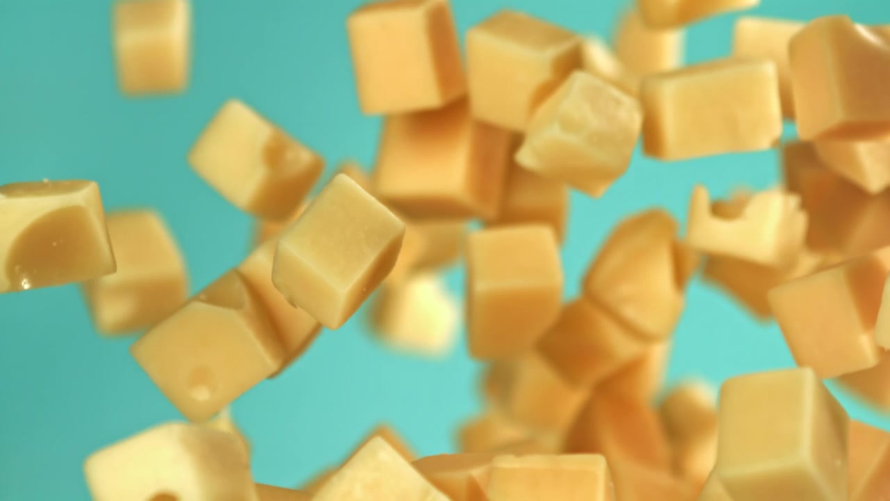 Dés de fromage tombant au ralenti sur un fond sarcelle