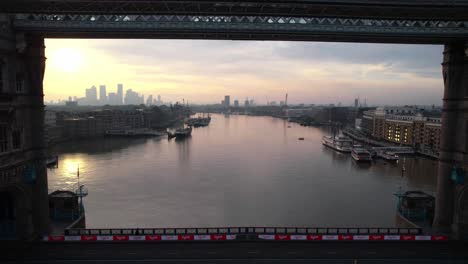 sensational aerial view of tower bridge in london, drone flying backwards at pink sunset sky, rises reveals uk's capital cityscape