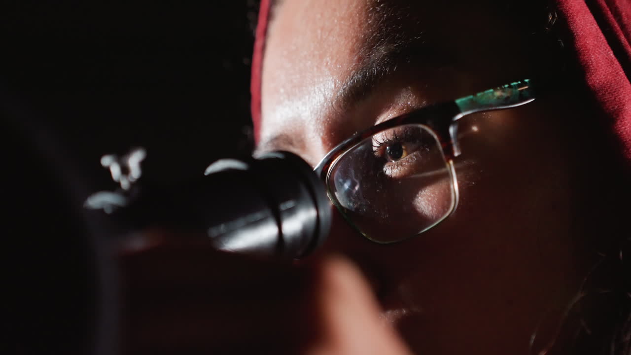 student astronomer peers through telescope at stars, dimly lit room, focused gaze behind glasses, adjusting eyepiece, capturing faint stellar details, scientific mood of quiet observation