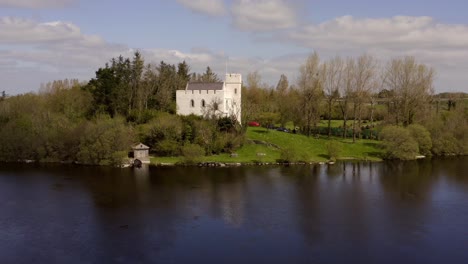pequeño castillo fortificado blanco con vistas al lago tranquilo desde el claro del bosque