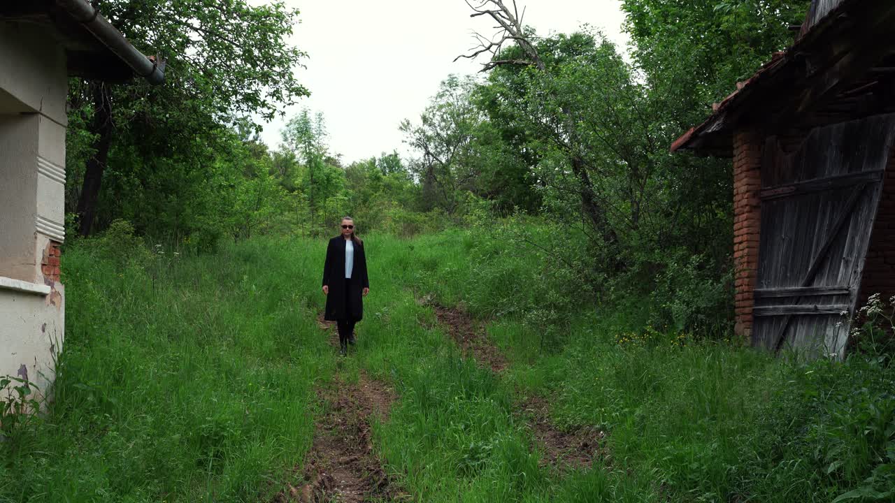 검은 옷을 입은 젊은 여성이 낡은 집을 지나간다