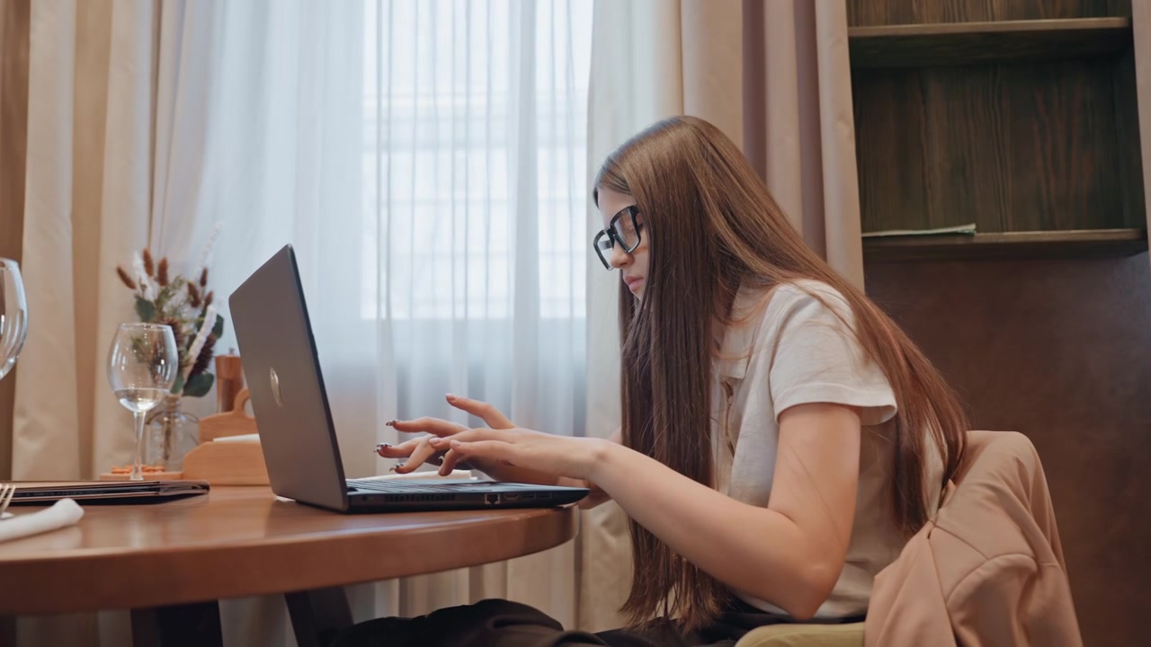 Giovane scrittore bianco che modifica contenuti su un laptop, intensamente concentrato con le dita sulla tastiera, appunti e un diario sparsi sul tavolo, un bicchiere di vino vuoto e un piatto di snack, calda luce solare pomeridiana che filtra attraverso la tenda.