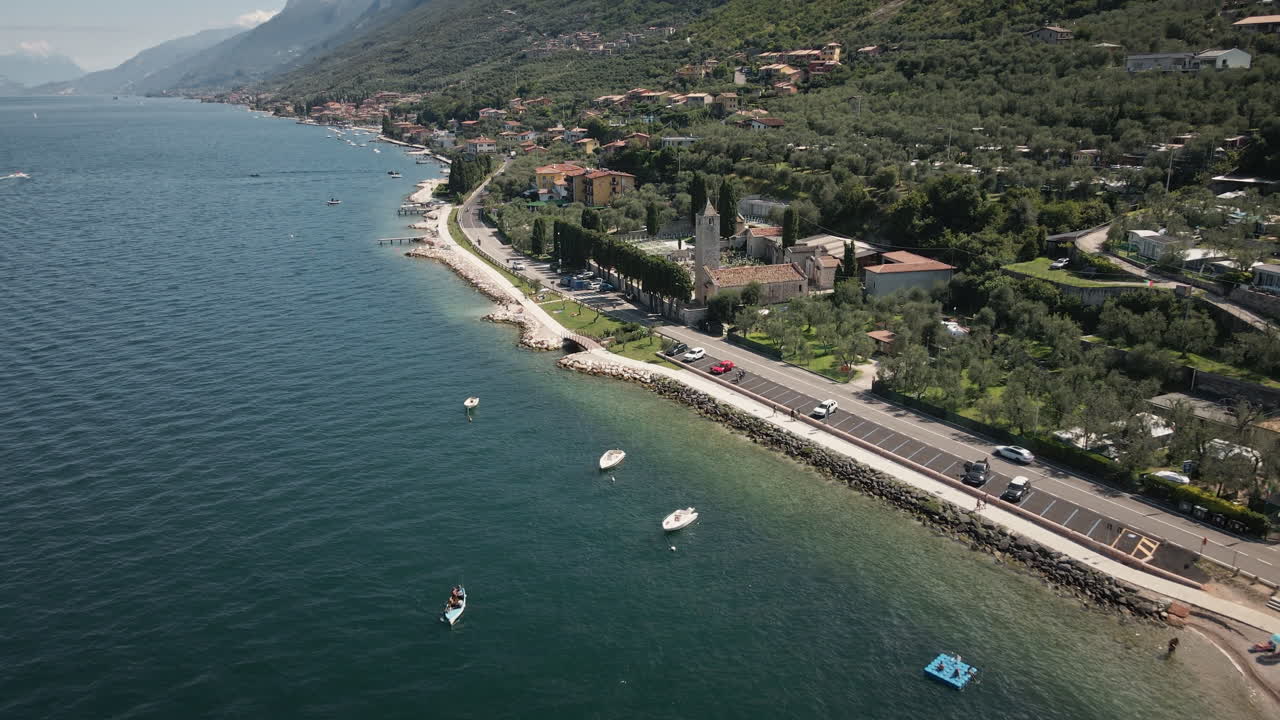 Drone 4K UHD fluido vola in avanti e si inclina verso il basso lungo una passeggiata sul lago con barche ormeggiate e acqua limpida, perfetto per video turistici, immobiliare e sfondi scenografici.