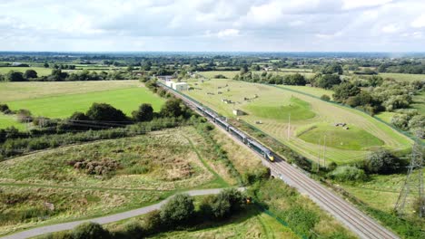 Train-driving-along-tracks-in-countryside-through-fields,-sunny-day