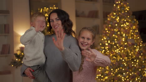 Mother,-Little-Girl-And-Boy-Looking-To-Camera-And-Waving-Hand-On-Christmas