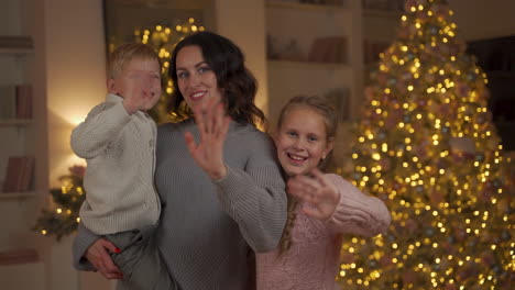 mother, little girl and boy looking to camera and waving hand on christmas