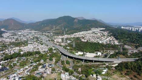 Vista-Aérea-De-La-Zona-Residencial-De-Las-Afueras-De-Hong-Kong,-Con-La-Autopista-De-Conexión-Y-Las-Laderas-De-Las-Montañas-Circundantes