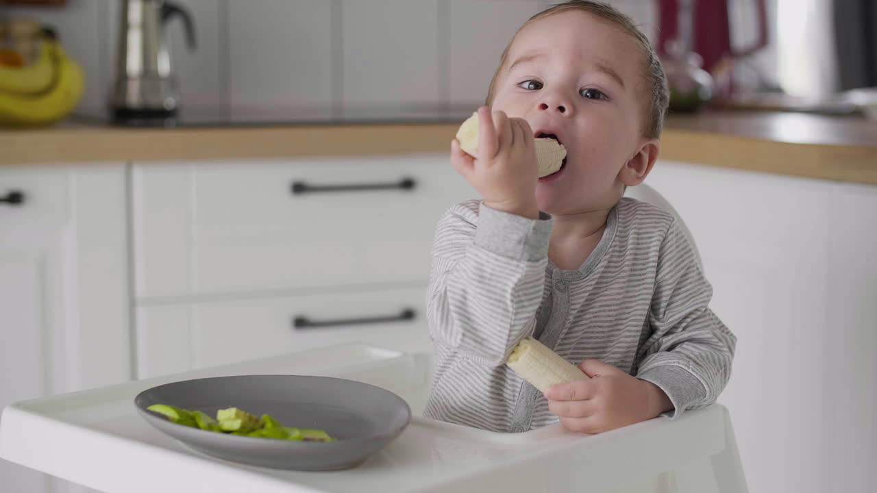 부엌에서 높은 의자에 앉아 바나나를 먹는 귀여운 아기 소년 1