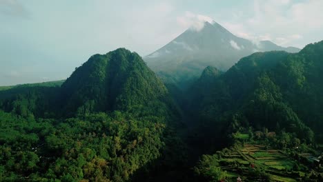 toma de dron dronie de selva tropical cubierta de vegetación en la colina con volcán en el fondo