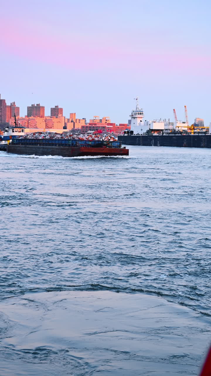 Loaded barges move by the riverscape. American flag flapping to the camera at foreground. Vertical video