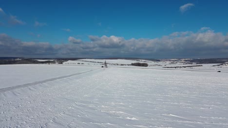 a-car-driving-on-a-snowy-road-between-fields-in-the-countryside,-which-is-all-white