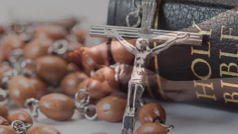 animation of caucasian woman praying with rosary over cross and bible