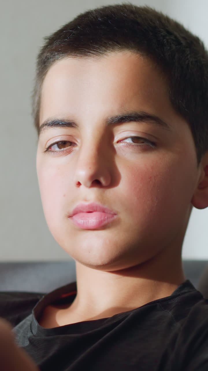 Boy sitting on a couch holding tea cup close to mouth, staring at the camera with a tired, sickly expression, conveying a sense of illness or discomfort while resting