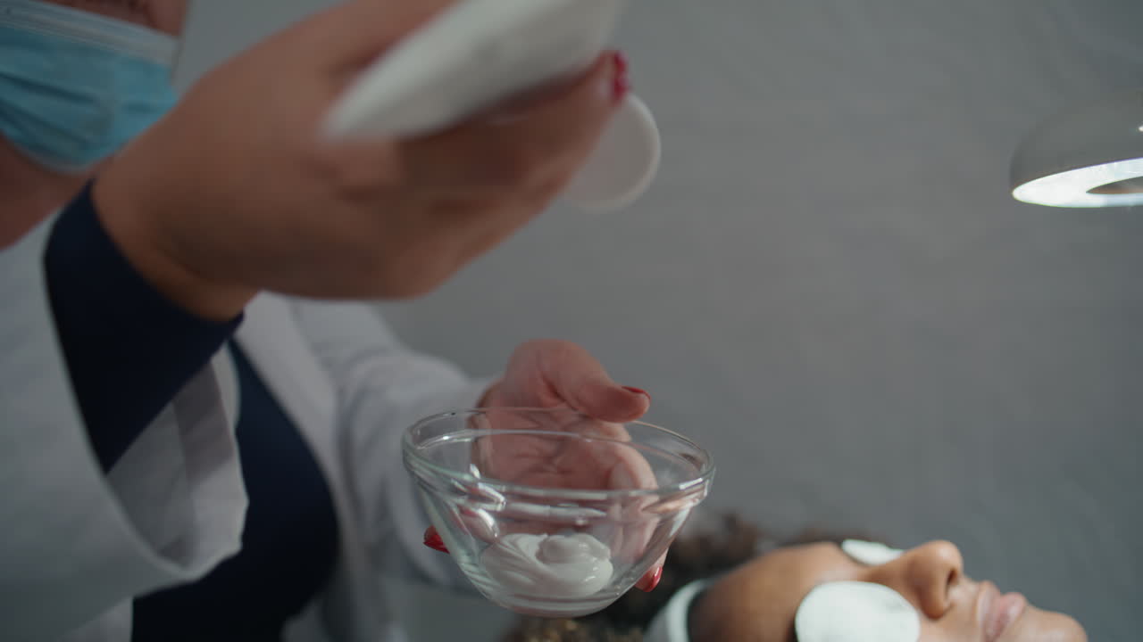 médico de primer plano exprimiendo crema de tubo en un frasco. manos preparando cosméticos para el cuidado de la piel