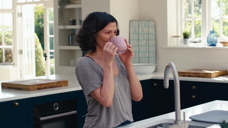 Smiling-Mature-Woman-Standing-In-Kitchen-Relaxing-With-Cup-Of-Coffee