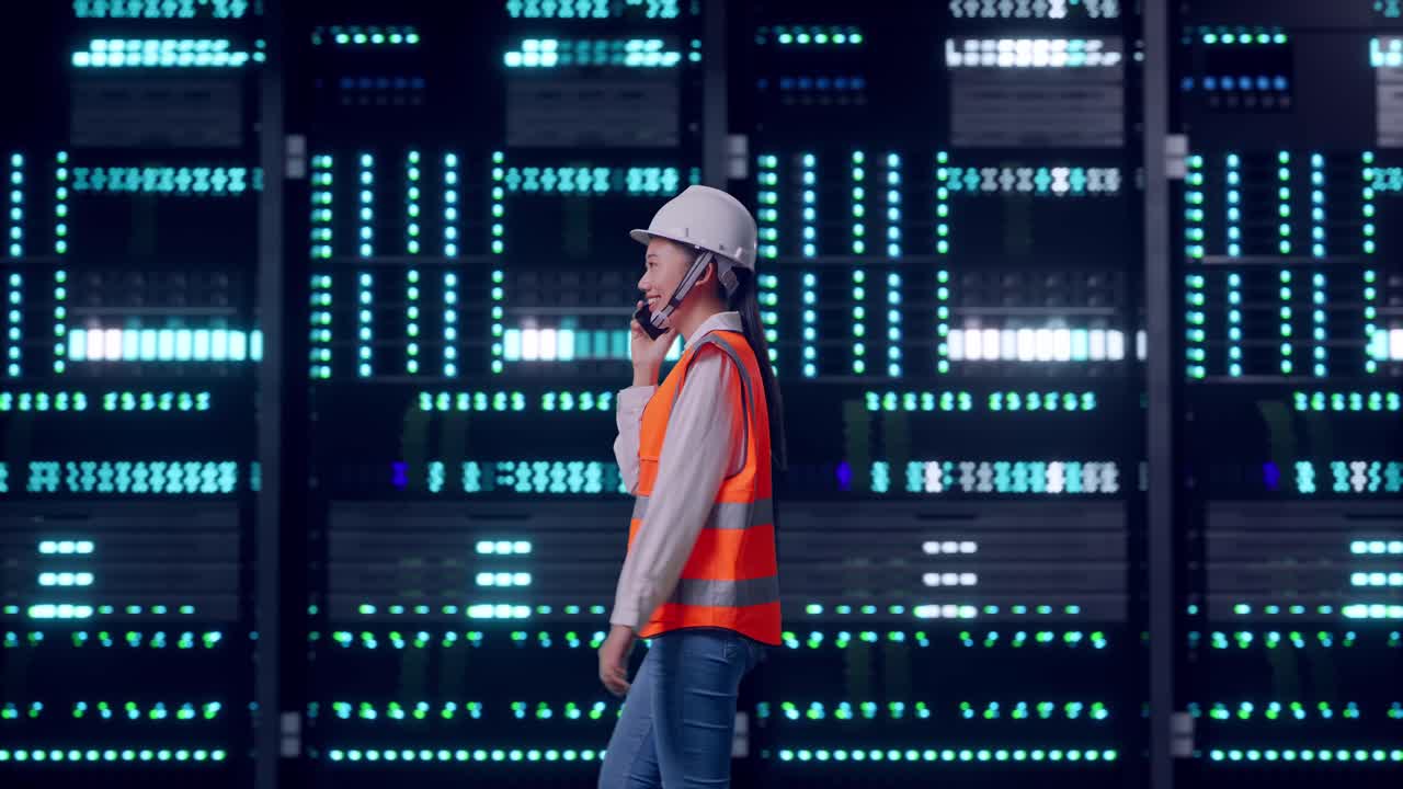 Side View of Asian Female Engineer Talking On Smartphone While Walking in Server Room Data Center