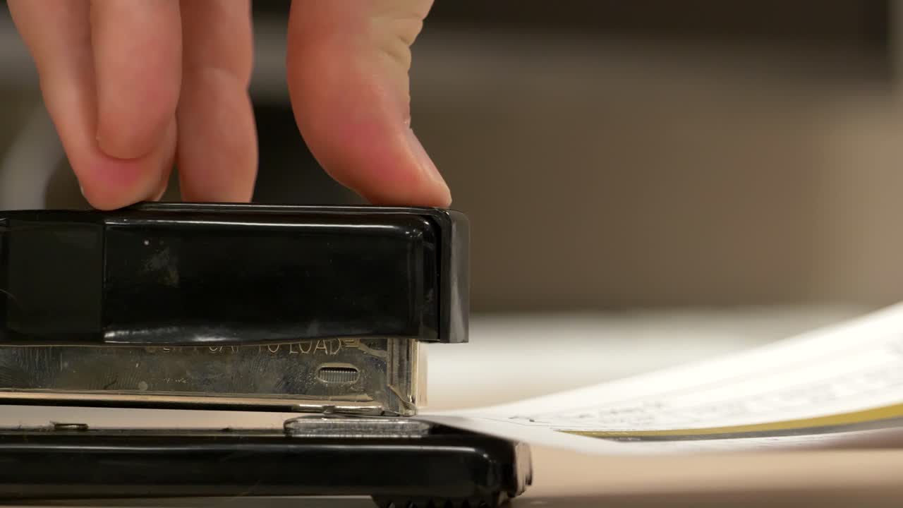 A close up from the side of a black stapler stapling pieces of paper together