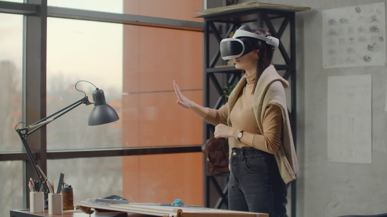 mujer moderna ingeniera-diseñadora en la oficina con grandes ventanas se encuentra en un casco de realidad virtual utiliza gestos para administrar el proyecto sin salir de la oficina. control de construcción. proyecto de diseño del edificio y el interior.