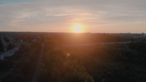 slow scenic aerial flight over train tracks outside nepean city, ontario at sunrise with the sun shining over the hill and trees