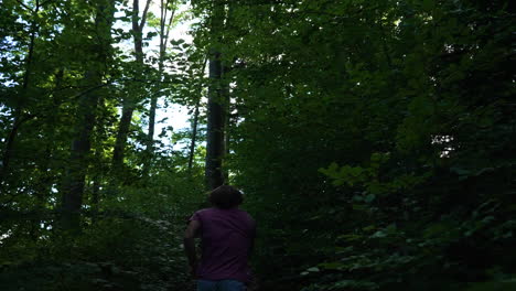 Young-man-with-red-tshirt-is-running-up-a-small-path-in-a-dark-forest-in-slow-motion