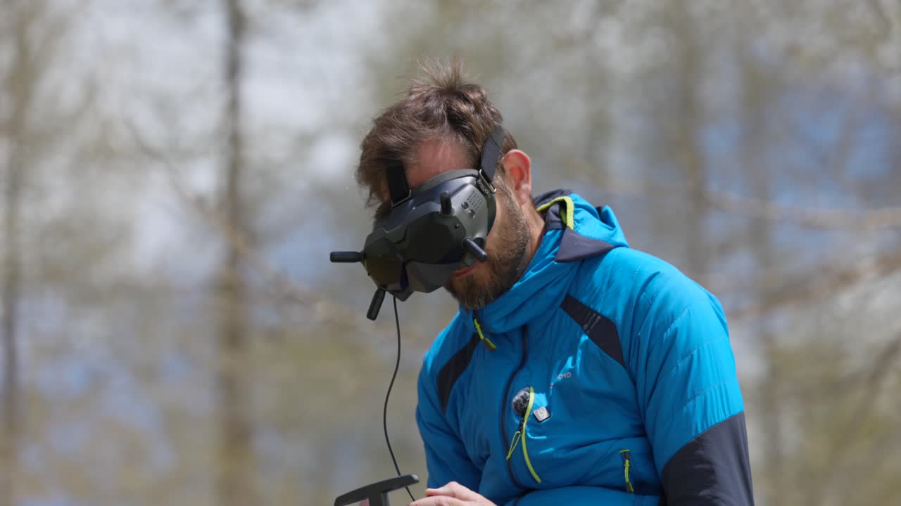 hombre con chaqueta azul usando un auricular de realidad virtual y control remoto para navegar un dron en un entorno al aire libre