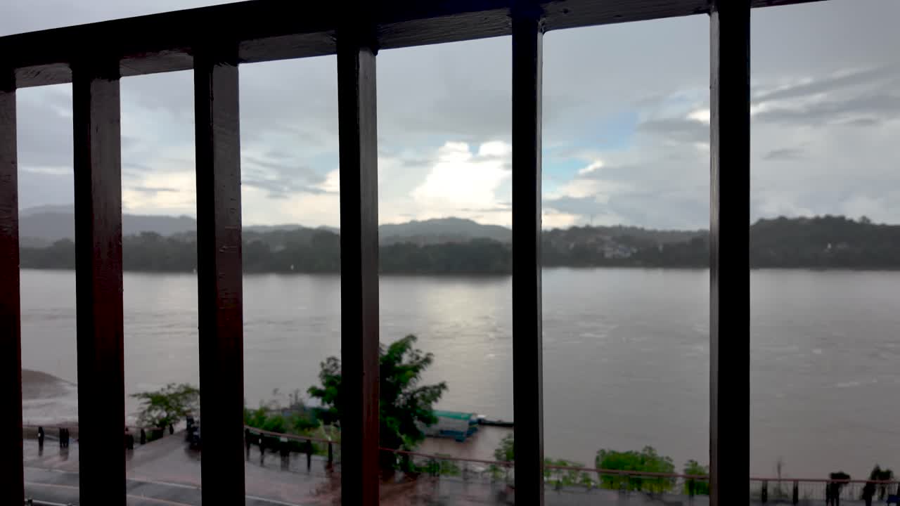 Metal railing framing a view of the Mekong River and mountains of Laos under an overcast sky