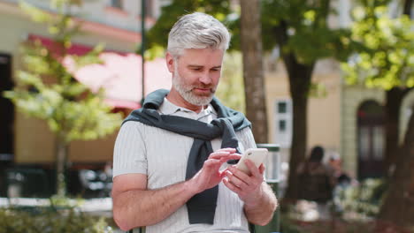 Mature-man-using-smartphone-typing-text-messages-internet-social-media-web-app-looking-up-thinking