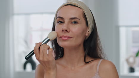 mujer feliz aplicando polvo retrato en casa. mujer sonriente rutina de maquillaje en el baño