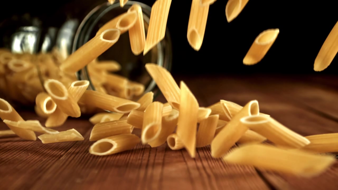 Penne secche che cadono su un tavolo di legno rustico