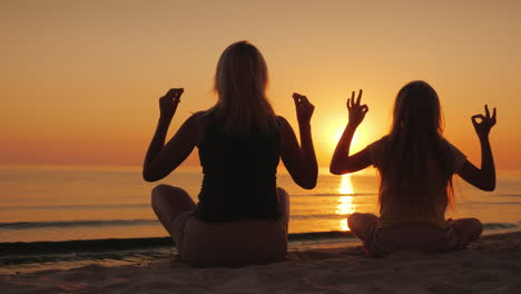 mom and daughter are meditating by the sea at sunset health and happy time together