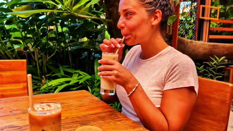 a young woman drinks an ice-cold cocktail on a terrace by a tropical garden