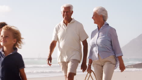 Grandparents-And-Grandchildren-Walking-Along-Beach-Carrying-Picnic-Basket