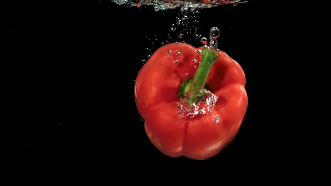 Červená paprika padající do vody s bublinkami na černém pozadí