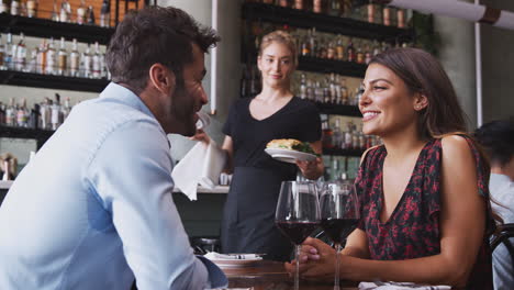 female waitress serving food to romantic couple sitting at restaurant table