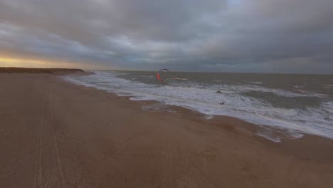 toma aérea de alta a baja de un kitesurfer durante la puesta de sol