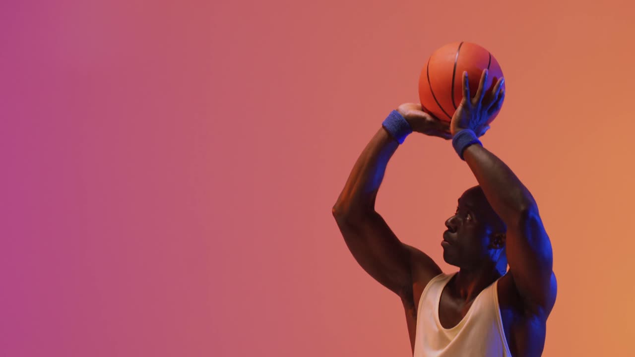 video de un jugador de baloncesto afroamericano lanzando una pelota sobre un fondo de color rosa a naranja