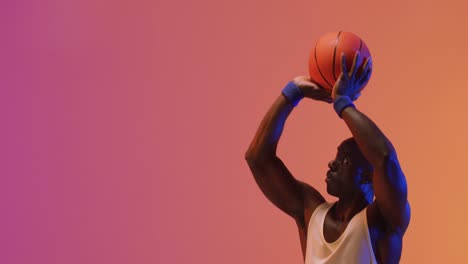 Video-of-african-american-male-basketball-player-throwing-ball-on-pink-to-orange-background