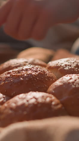 a close-up of freshly baked sesame seed bread rolls placed on a blanket in a grassy field. children's hands are seen reaching towards the bread, creating a warm and inviting picnic atmosphere