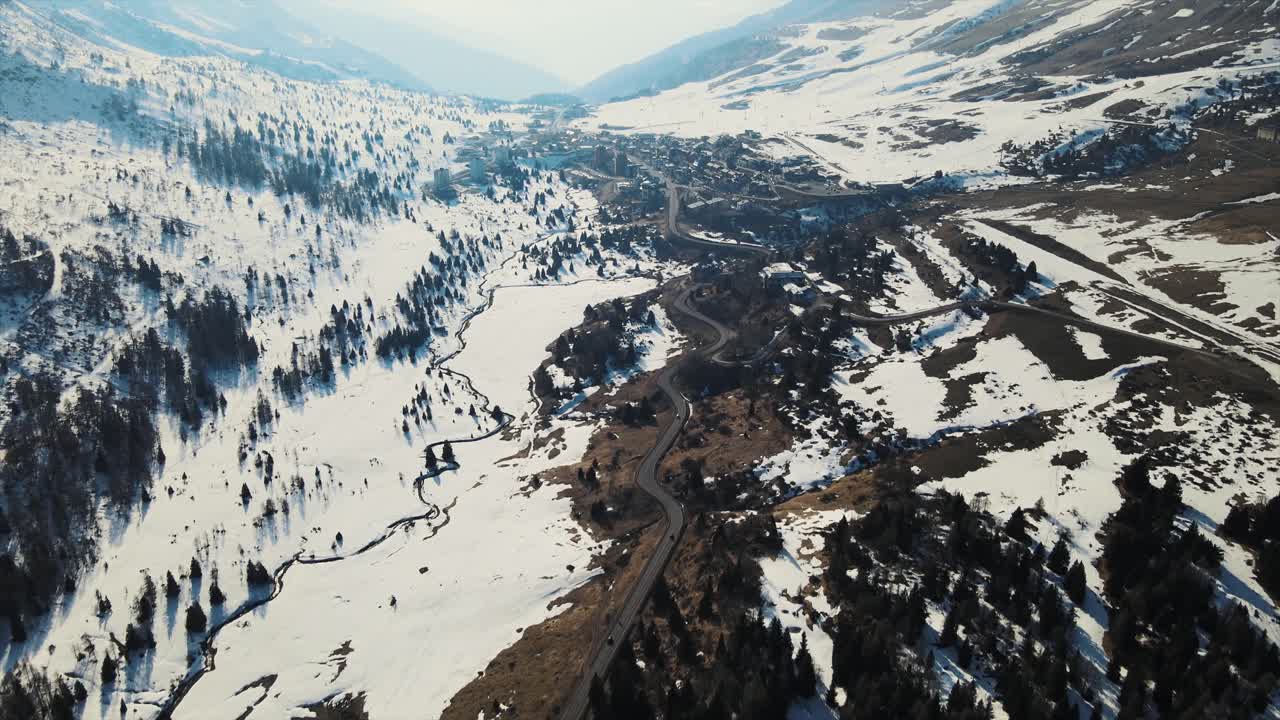 Aerial drone shot of a winding road cutting through a snowy mountain landscape